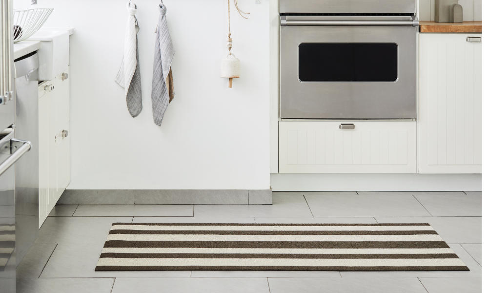 A neat kitchen floor image featuring a shag floor mat with multi stripes in brown and beige. some kitchen appliances in the background