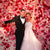 A couple on their wedding day, smiling and excited with a wall of stunning pink and red roses in the background