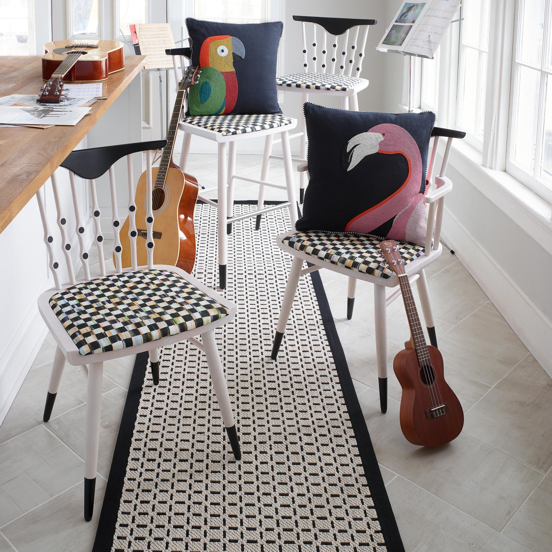 Four Counter stools, two colorful pillows with a flamingo and a  parrot, and three guitars in the room.