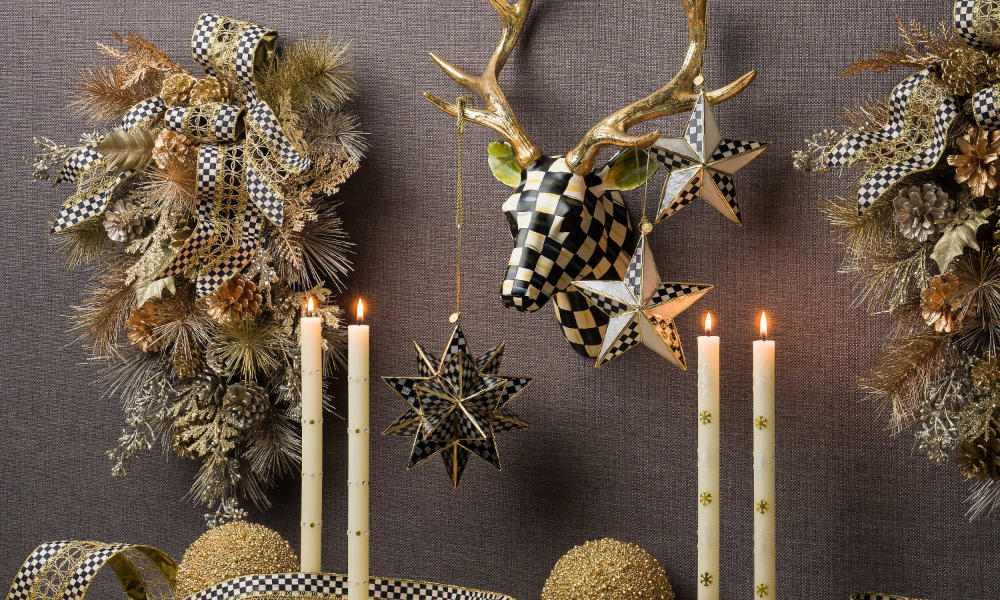 Two holiday wreaths on a wall, a beautiful courtly check deer, with some holiday ornaments, and a couple of Christmas candles on a table