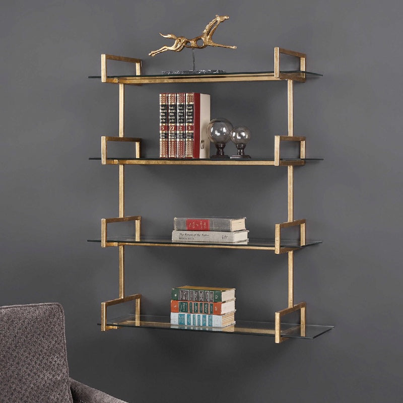 A four-shelves gold finish wall shelf, hanging on a grey wall, with books on the three bottom shelves and a gold horse sculpture on the top shelf.