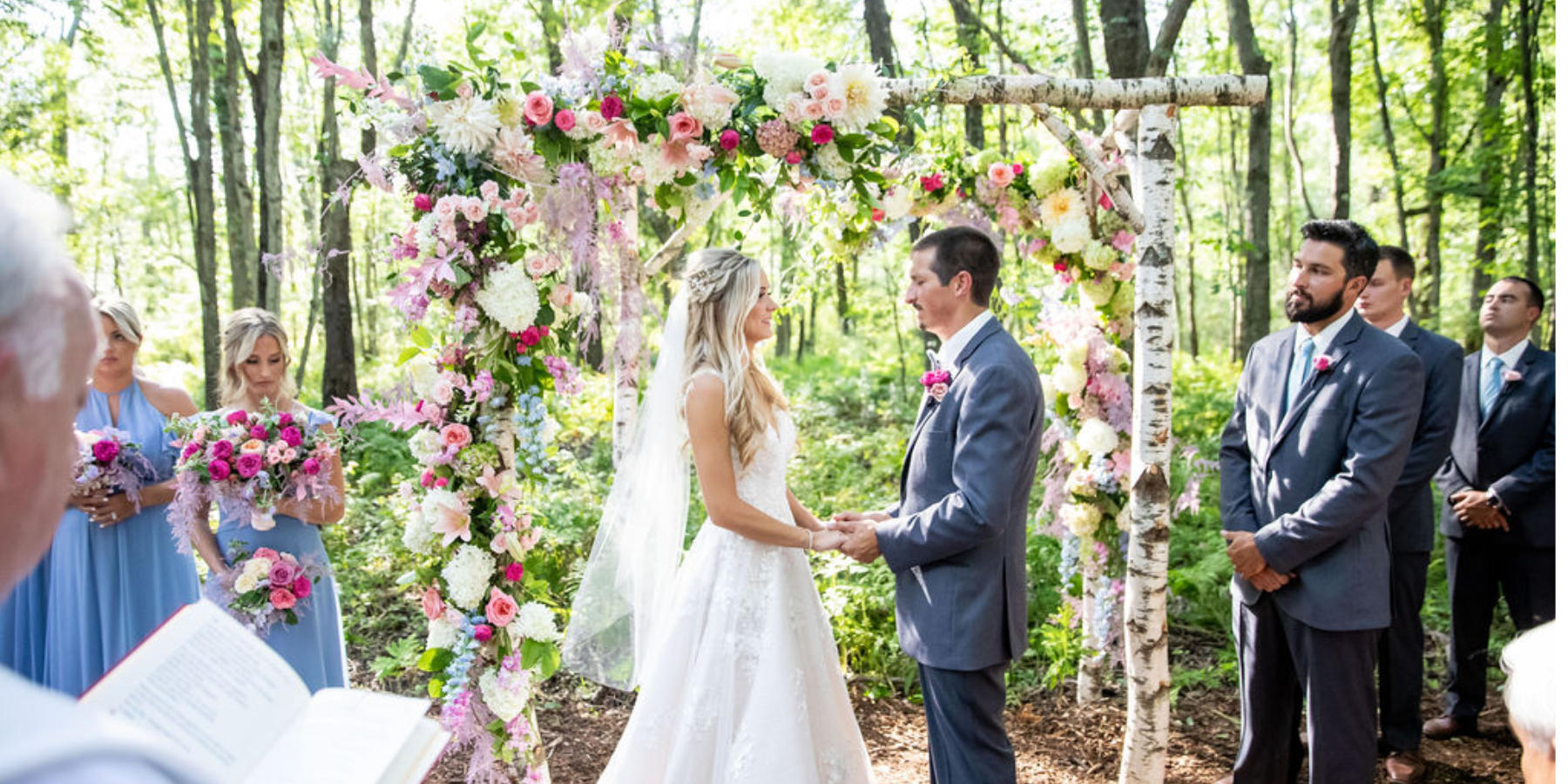An altar for a wedding in the woods, the couple is standing under a stunning arbor with colorful and beautiful flowers