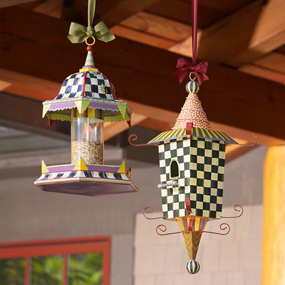A colorful birdhouse, and a bright bird feeder, hanging from a gutter.