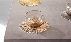 Three modern round coasters in gold, silver and brass metallic colors on a corner of a dining table, two empty glasses on top of two of them