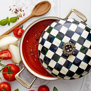 Courtly check enamel casserole filled with a tomato sauce with a very vivid and deep red color, some tomatoes and onions are on the table and a wooden spoon.