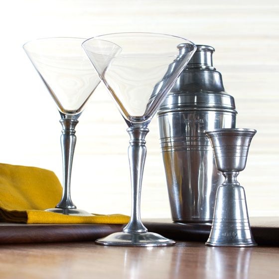 Martini glasses set, a cocktail shaker and a jigger, next to a mustard color cloth napkin 