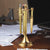 A golden desktop set that includes a letter opener and two pencil holders, on the background some blurry papers and notepads.