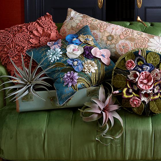 A green couch, with different pillows and cushions in very vivid colors and flowers details.