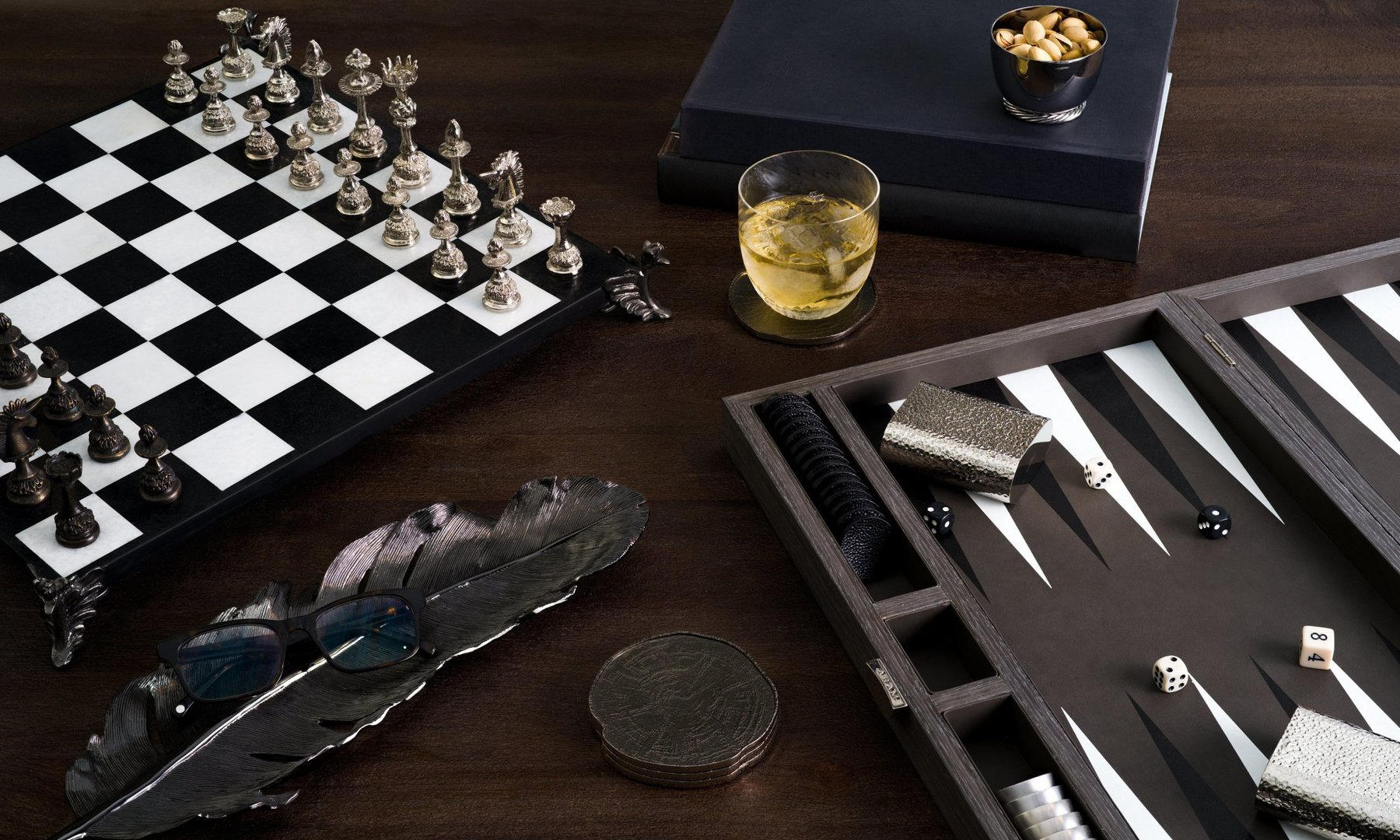 A wood table with a chess and a backgammom game, a shot glass and a small bowl with nuts