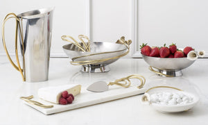 A neat table presentation, with a bowl with beautifully arrange strawberries, a cheeseboard with bree cheese, 2 more bowls and a water pitcher, all with gold accents