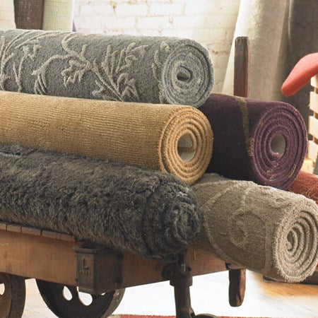 A pile of five hand-knotted rugs on a wood rolling box, the rugs are presented in different colors and patterns.