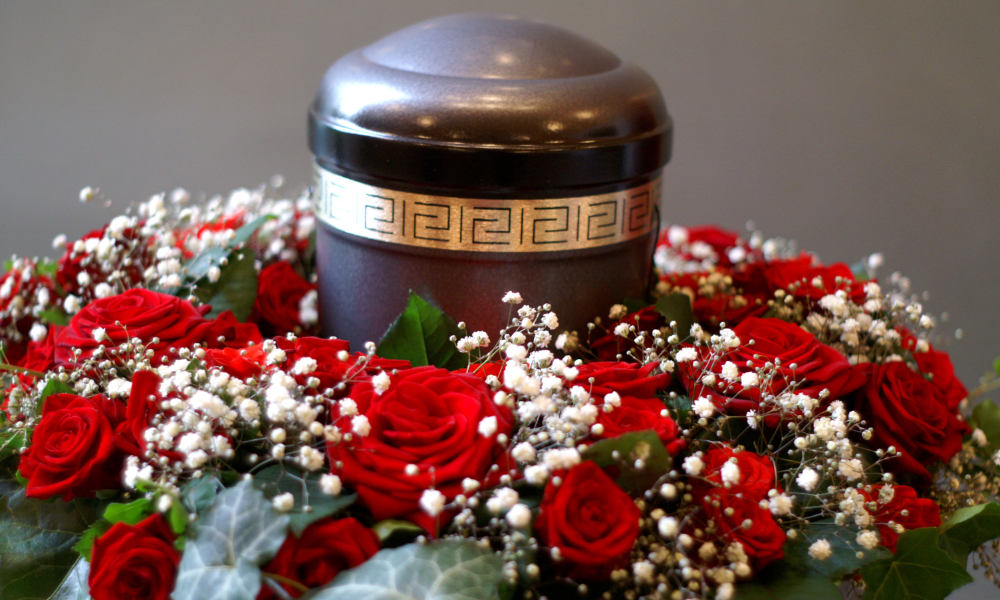 A urn tribute in bronze with a golden ring and beautiful red roses around it