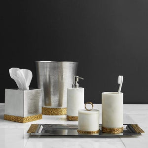 A set of bathroom accessories, including a toothbrush cup, a canister, and a soap dispenser, in white with an antique gold finish at the bottom. There's also a wastebasket and a tissue box in silver with the same gold finish.