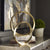 Two golden ring sculptures and a small plant on top of a shiny finish console table, on the wall, there is abstract wall art with gold, brown and blue tones.