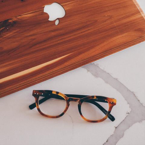 Brown frame readers on a white countertop, and an macbook laptop with a brown case that match the readers color.