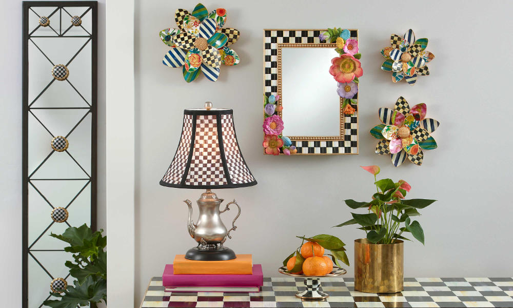 A Colorfull set up for a wall with a mirror and three decorative objects, also a table lamp enhancing the scene.