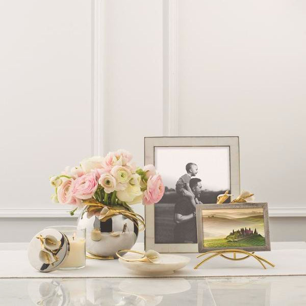 A Silver picture frame shows a man carrying a kid on his shoulders, and a golden frame containing a landscape picture. Next to it a vase with a beautiful flower arrangement.