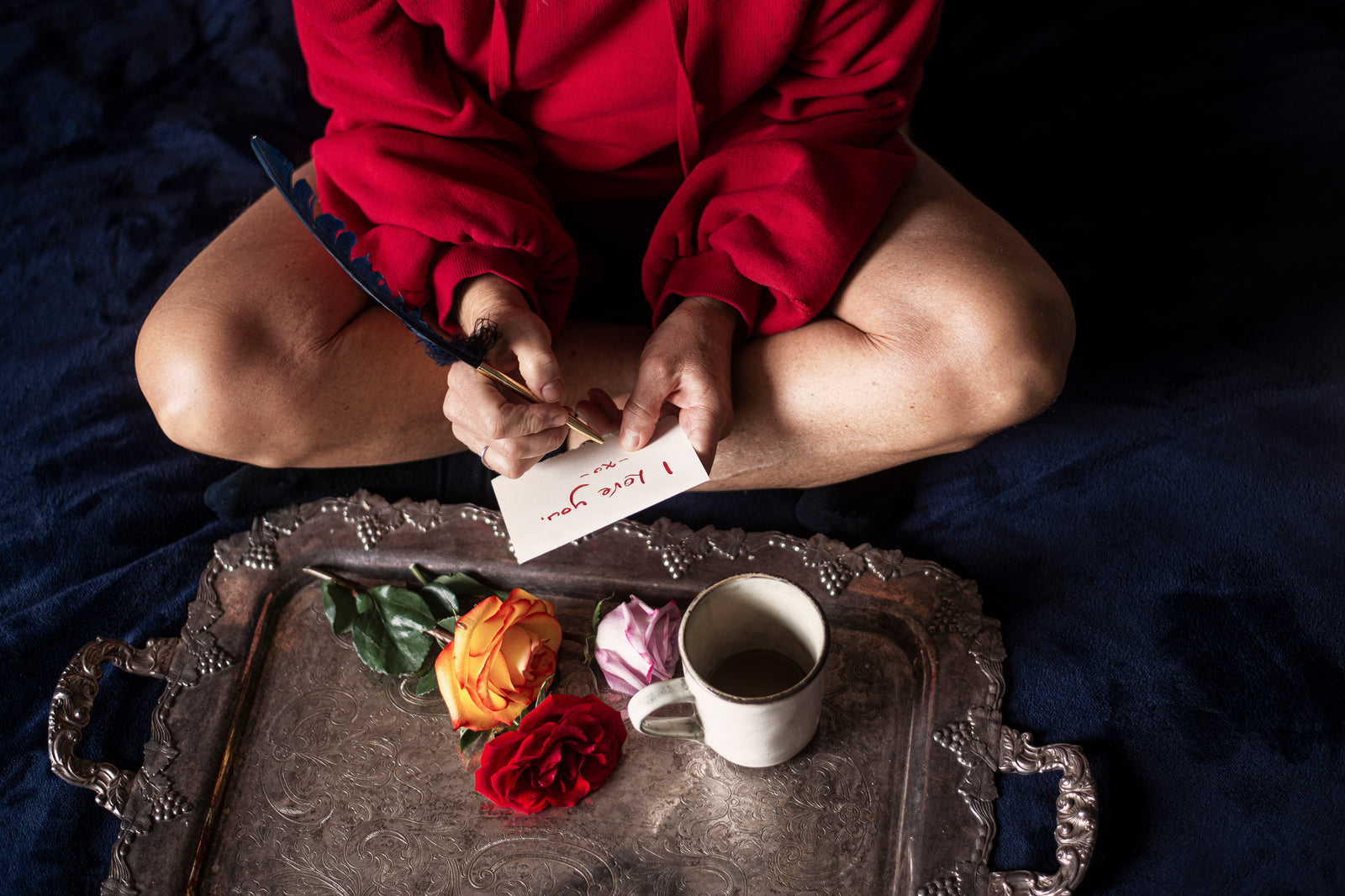 A girl is writing a note to someone she loves, she is seating on the floor next to a try with some roses on it