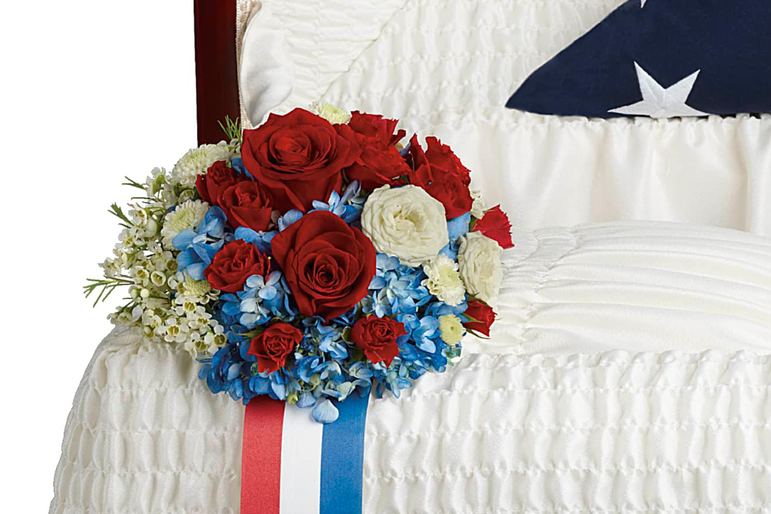 A casket insert made of Blue hydrangea, red roses, red spray roses, white spray roses, white button spray chrysanthemums, and white waxflower are accented with galax leaf. This beatufil funeral flower arrangement is over the corner of the opened casket