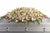 A casket spray made with whit and light pink roses on top of a grey casket