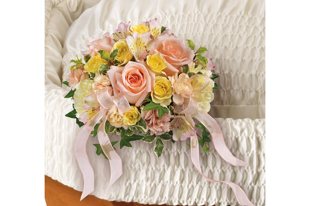 A Gorgeous bouquet of peach roses are arranged with light yellow spray roses, pink alstroemeria, light yellow carnations, miniature peach carnations, pitta negra and variegated ivy. This funeral flowers are hanging on the corner of the casket