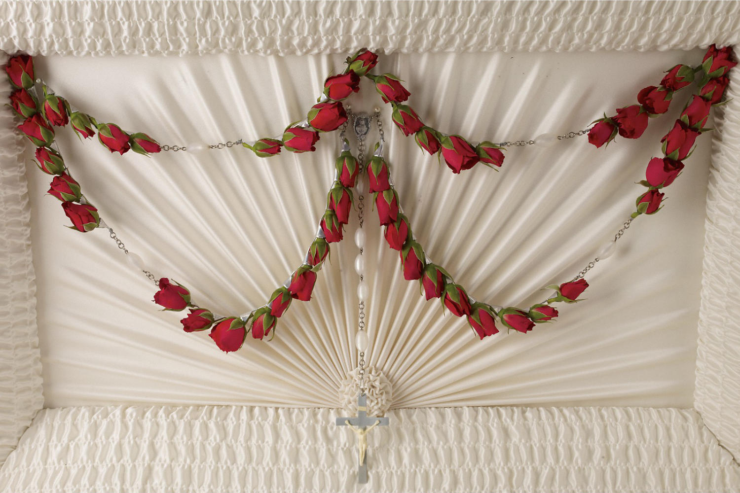 A rosary made of 50 red roses hanging from the inside side of a casket for a funeral set up